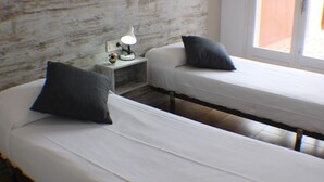 Deux lits simples avec du linge de lit blanc et des oreillers foncés, dans une chambre dotée d’une tête de lit en bois rustique.
