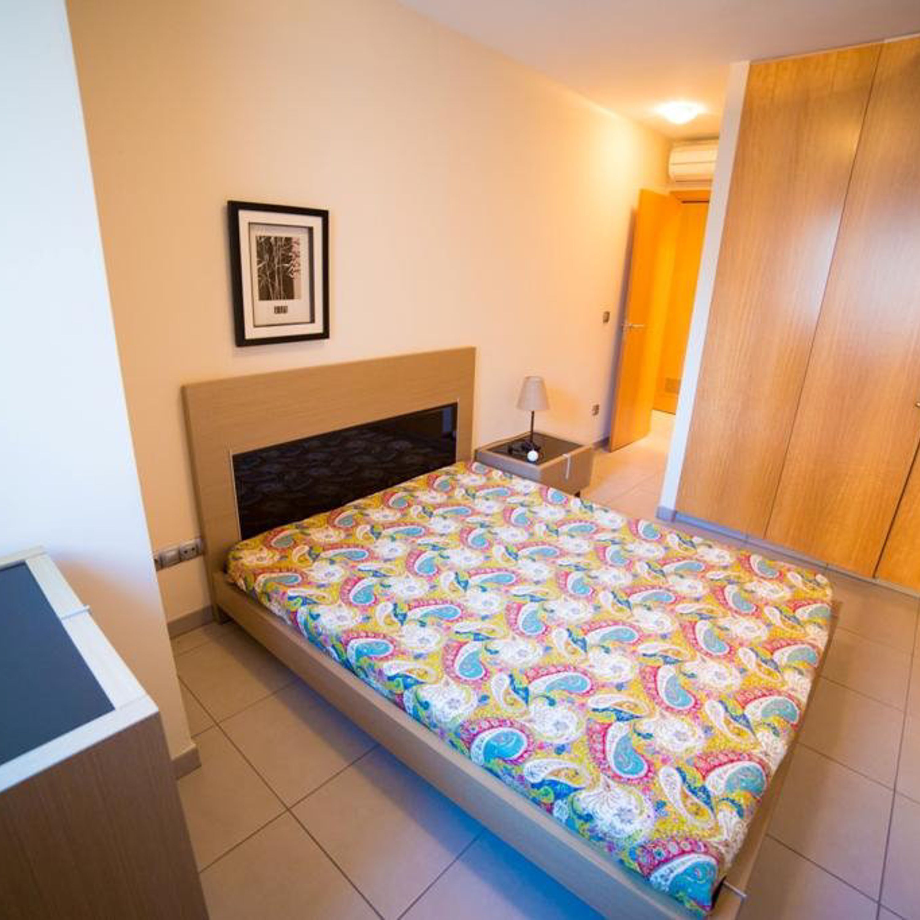 A bedroom with a bed, a bedside table, a lamp, a framed picture on the wall, and a wardrobe.