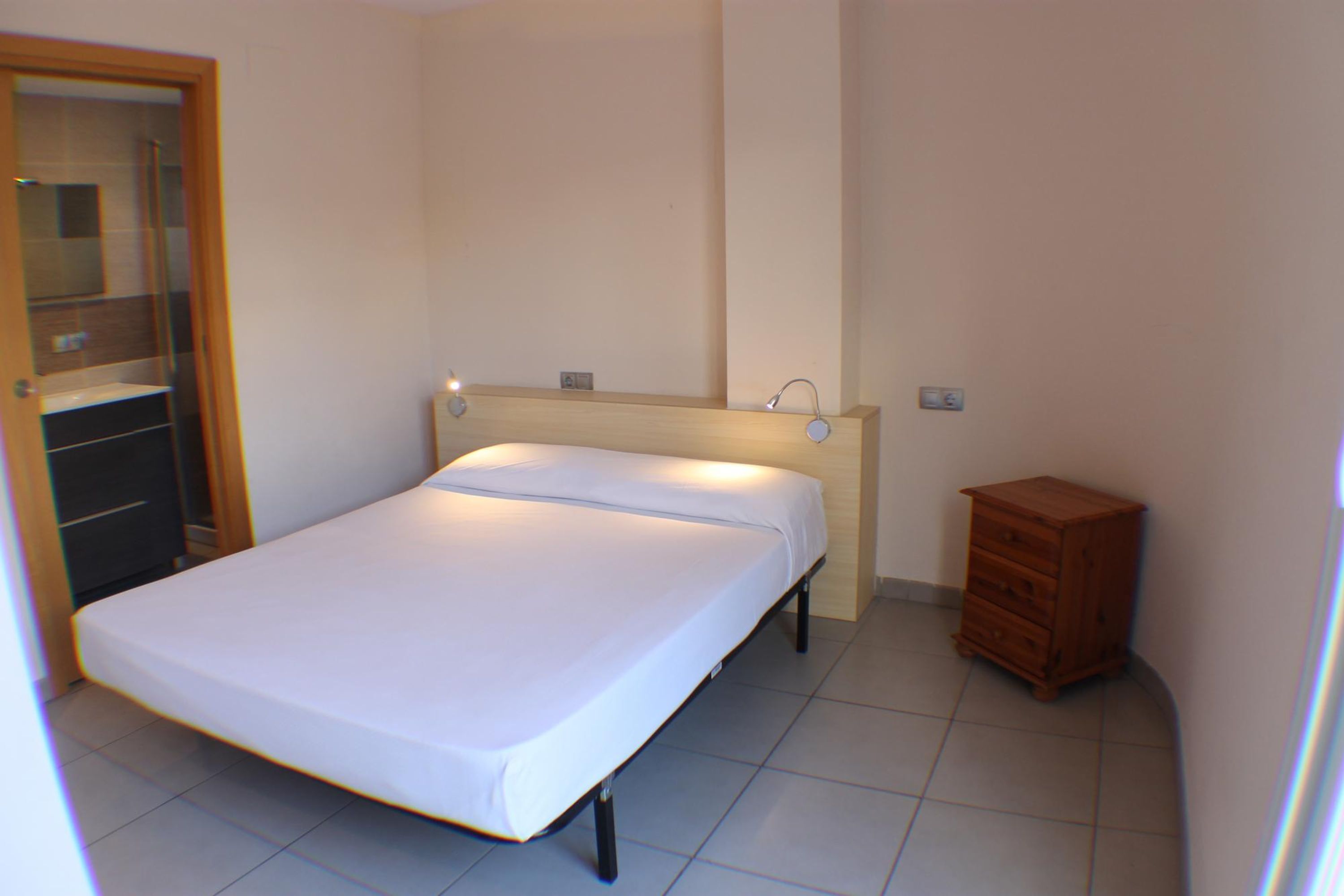 Un dormitorio con una cama, un aparador de madera y un baño visible a través de una puerta abierta.