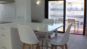 A modern kitchen with a dining area, white cabinetry, and a view of a balcony with outdoor furniture.