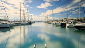A marina with boats docked along the water's edge, a wooden dock in the foreground, and a clear sky above.