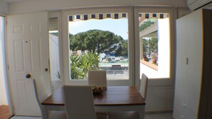 Un comedor con mesa y sillas, vista al mar y un árbol, y un balcón con plantas en macetas.