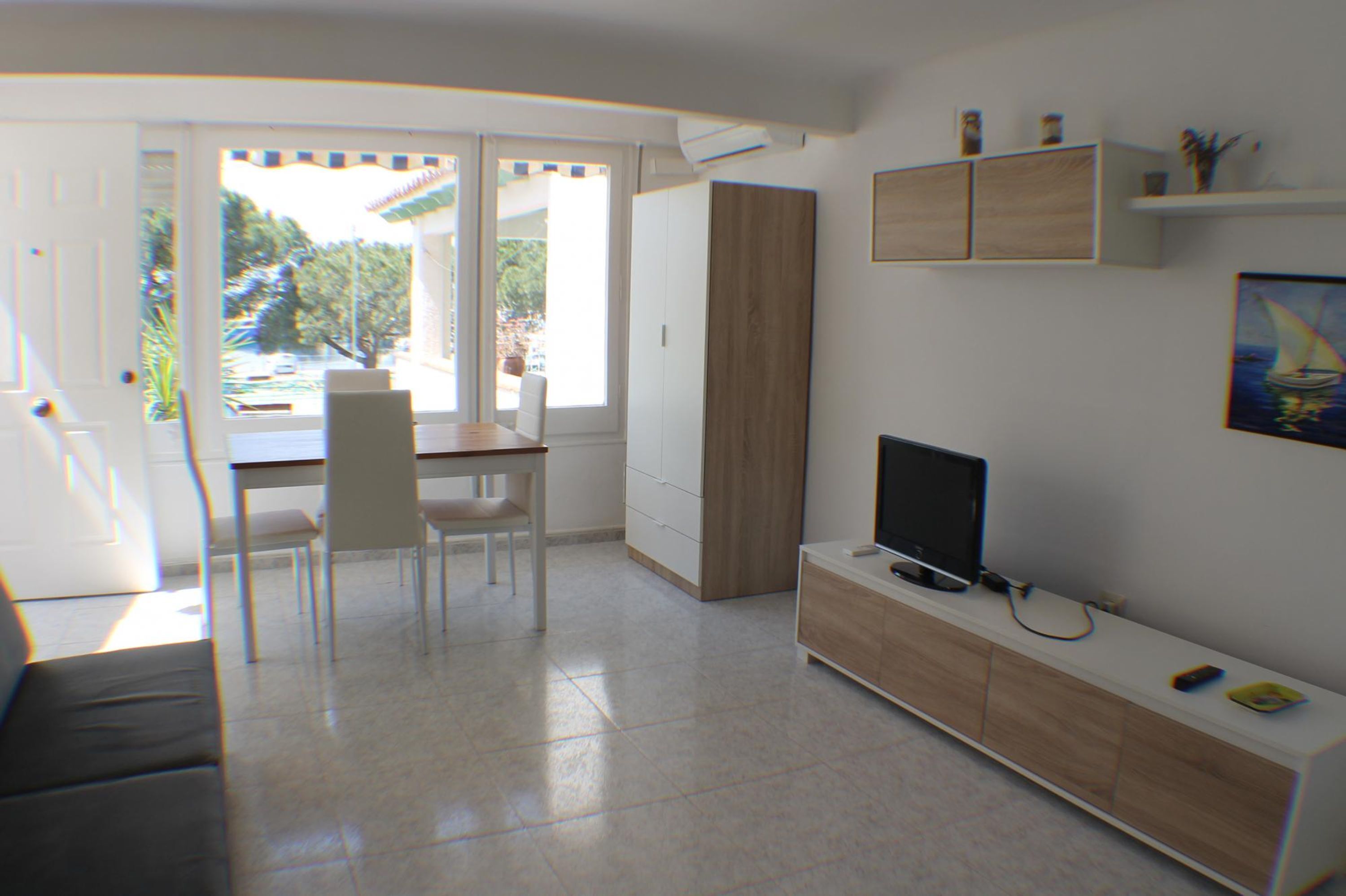 Un soggiorno moderno con zona pranzo, televisore e porta scorrevole in vetro che dà su un balcone.