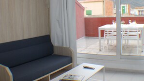 A room with a dark blue sofa, a white coffee table, and a large sliding glass door leading to an outdoor patio with a table and chairs. - Pi Sunyer 4 4C in Roses (Roses)