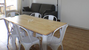Zona pranzo con tavolo in legno e sedie bianche, un divano grigio e una lampada da terra.
