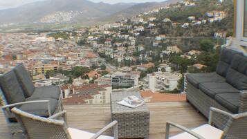 Un balcon agrémenté de meubles en osier, offrant une vue sur un paysage urbain avec des bâtiments et des montagnes en arrière-plan.