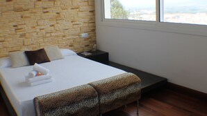 A bedroom with a bed, a bench, a nightstand, and a window with a view. - Villa Pamela in Roses (Roses)