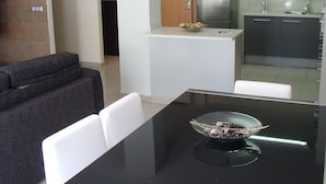 Une cuisine moderne avec un plan de travail noir, des chaises blanches et un saladier rempli de fruits.
