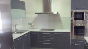 Une cuisine moderne avec des meubles gris, un réfrigérateur en acier inoxydable, un four à micro-ondes et un four traditionnel.