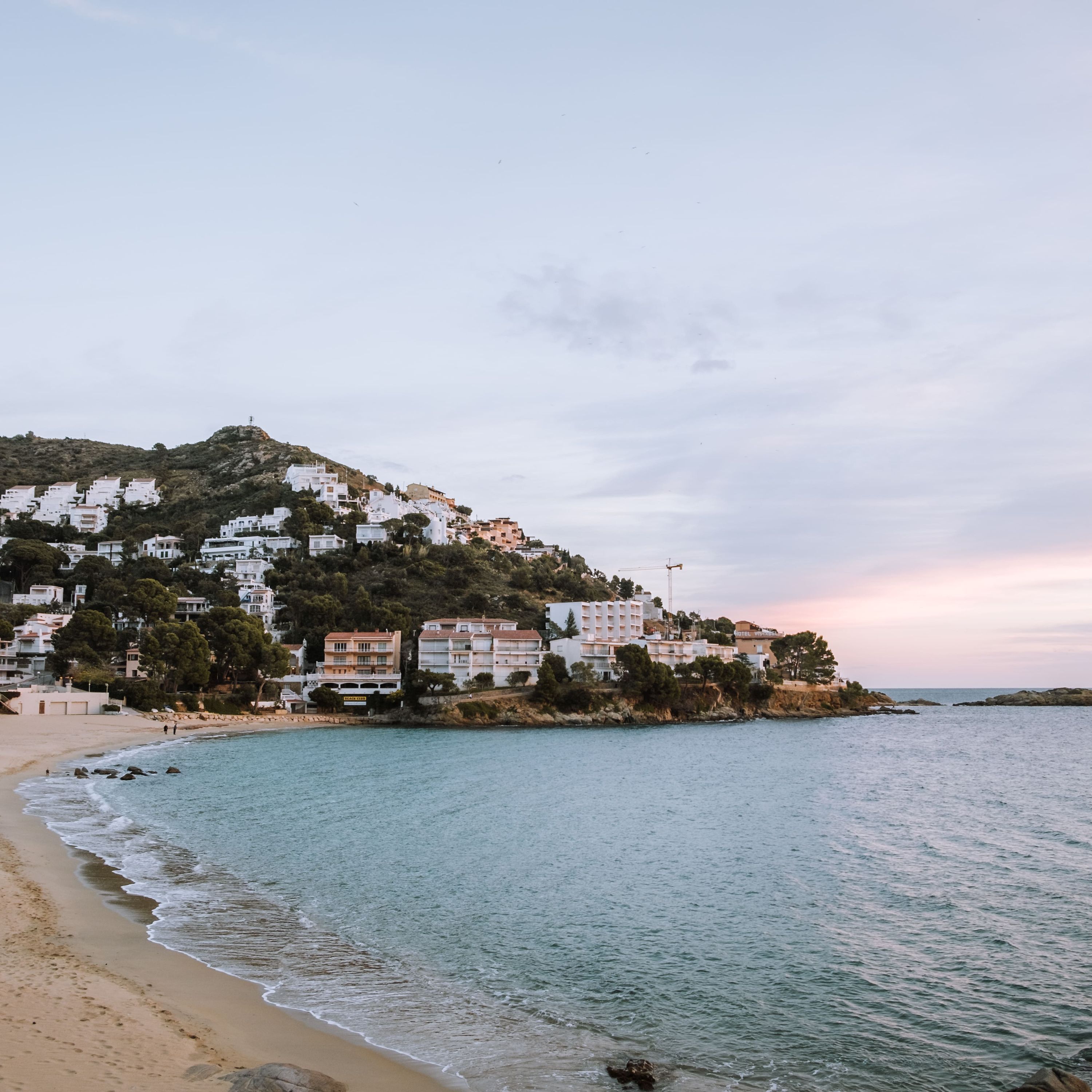 A coastal town with buildings on a hillside, a beach, and calm sea.