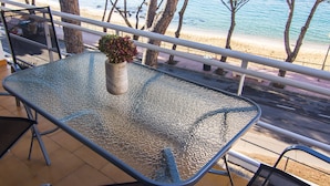 Un tavolo in vetro con sedie in metallo, una pianta in vaso e vista sulla spiaggia e sugli alberi.