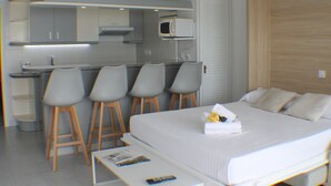 Habitación de hotel compacta con cama, un pequeño escritorio y una kitchenette con microondas y taburetes de bar.