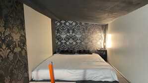 A small, narrow room with a bed, a nightstand, and a wall-mounted light. - Close to the Eiffel Tower, tiny triplex apartment on the banks of the Seine in Paris.  (Paris)