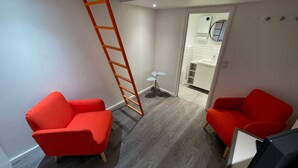 A modern room with two red chairs, a wooden ladder, and a view into a bathroom. - Close to the Eiffel Tower, tiny triplex apartment on the banks of the Seine in Paris.  (Paris)