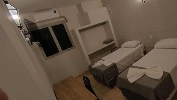 Une chambre d’hôtel avec deux lits simples, une petite table, une chaise, une armoire et une fenêtre.