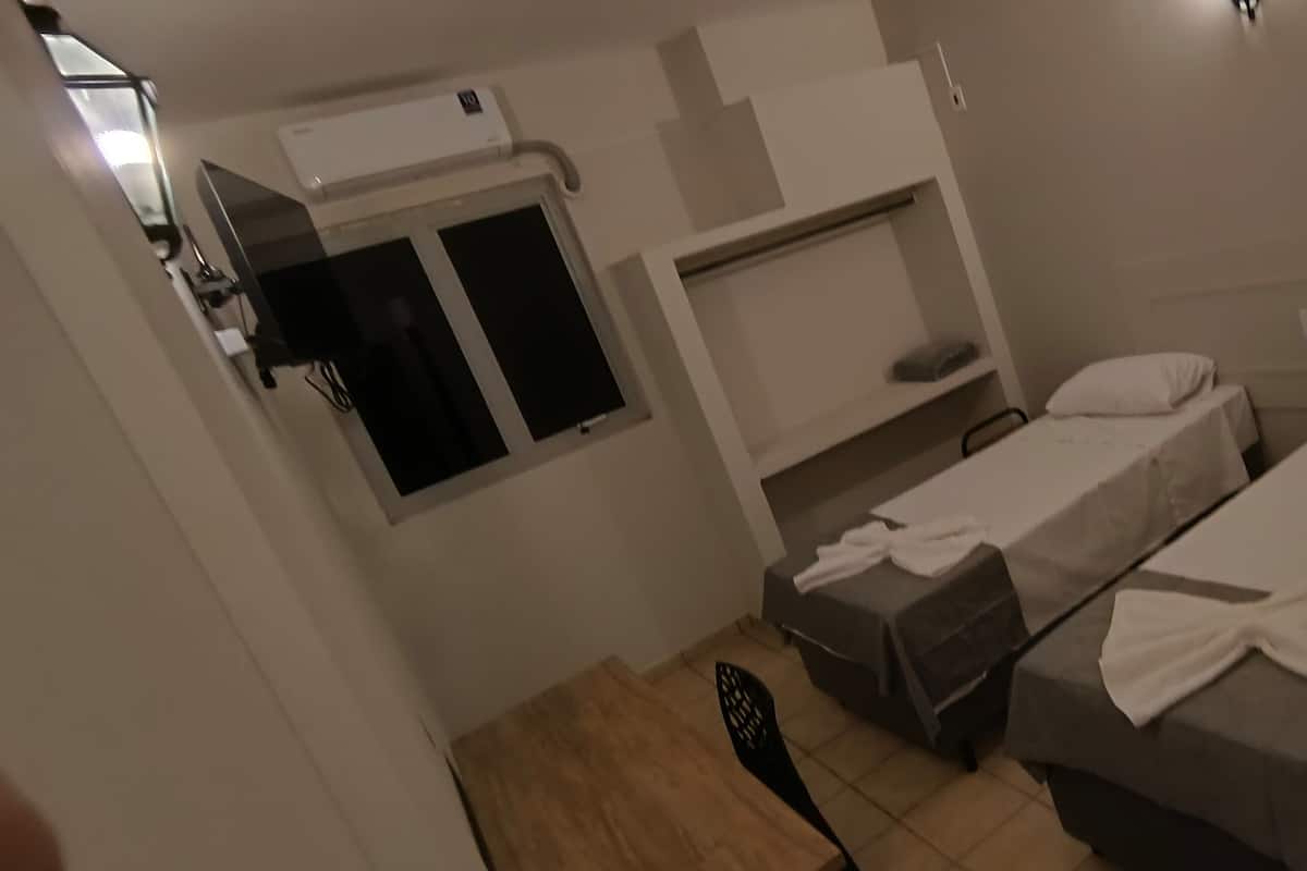 A hotel room with two single beds, a small table, a chair, a wardrobe, and a window.