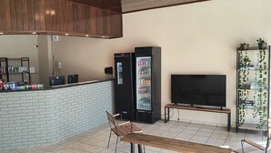 Un espace bar avec un comptoir en briques, deux réfrigérateurs remplis de boissons, un téléviseur à écran plat et un banc.