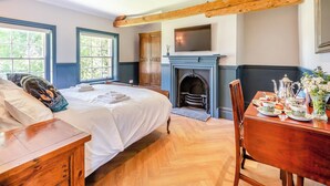 Ein Schlafzimmer mit einem Bett, Nachttischen, einem Kamin, einem Esstisch mit Tellern und einem Fernseher an der Wand.