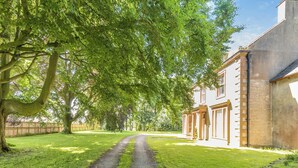 Ein gepflasterter Weg führt zu einem Gebäude im traditionellen Baustil, umgeben von üppigen Bäumen und einem gepflegten Rasen.