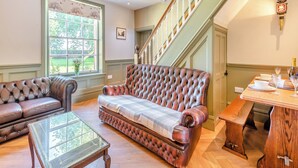 Ein geräumiges Wohnzimmer mit einer Ledersofa, einem Couchtisch mit Glasplatte und einem Essbereich mit Holztisch und Stühlen. Eine Treppe mit Holzwand verläuft zu einer oberen Etage.