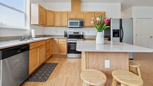 Una cocina moderna con armarios de madera, electrodomésticos de acero inoxidable, una isla central con taburetes y vistas al exterior.