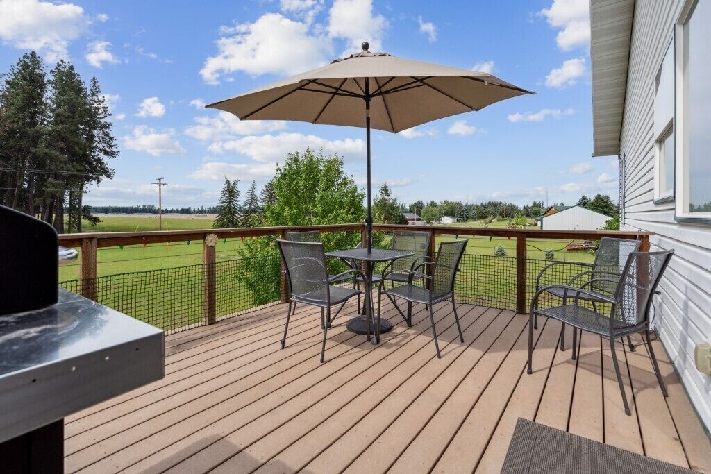 Una terraza de madera con una mesa, sillas, una sombrilla y una parrilla.