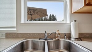 Una cocina con un lavamanos de acero inoxidable doble, una ventana con un paraguas y un rodillo de toallas de papel.