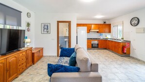 A living room with a TV, sofa, and wooden cabinets. There is a kitchen area with wooden cabinets and a refrigerator. - Cubo's Casa Rural El Andaluz / private pool / free wifi / BBQ (Coín)