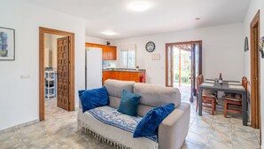 A living room with a sofa, a dining table with chairs, a kitchen in the background, and a door leading to another room. - Cubo's Casa Rural El Andaluz / private pool / free wifi / BBQ (Coín)
