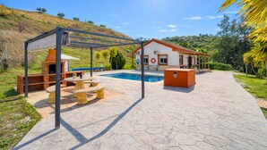 A poolside area with a pergola, outdoor seating, and a house with a red roof. - Cubo's Casa Rural El Andaluz / private pool / free wifi / BBQ (Coín)