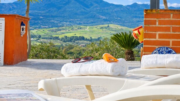 A sunlit terrace with a view of rolling hills and mountains, a brick wall, and a white lounge chair. - Cubo's Casa Rural El Andaluz / private pool / free wifi / BBQ (Coín)