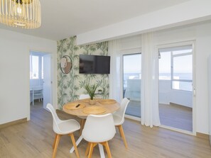 A modern dining area with a round table, white chairs, a mounted TV, and a view of the sea through large windows. - Cubo's Apartamento Algaida Calahonda Beach / beach access / free wifi / terrace (Mijas Costa)