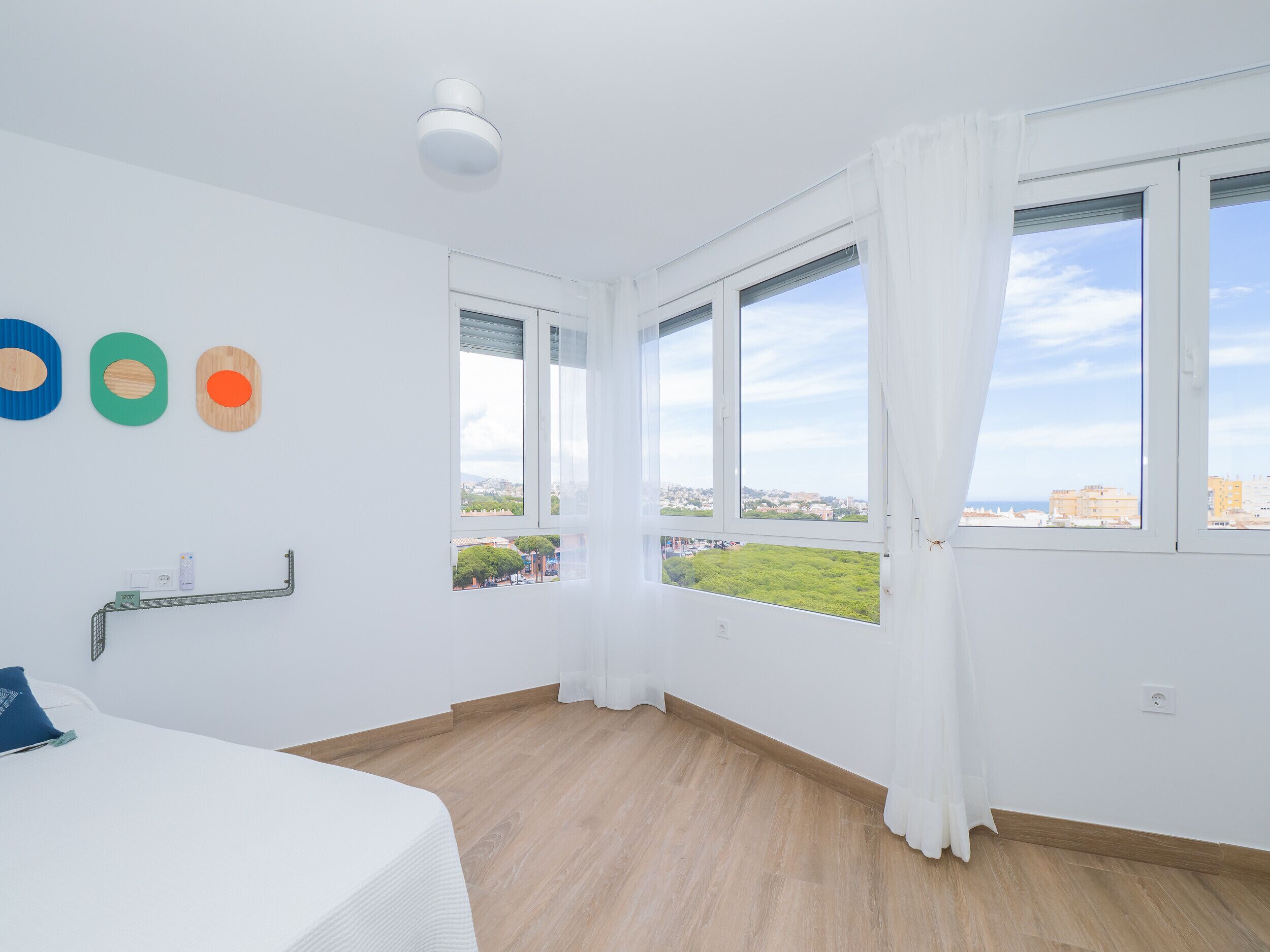 Una habitación con cama, ventana con cortinas, luz de techo y un muro con tres adornos circulares.