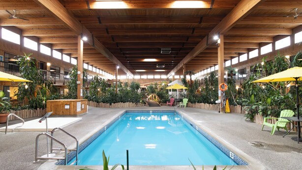 An indoor swimming pool with wooden beams, green chairs, and yellow umbrellas. - Home Away From Home (Prince George)