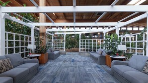 A covered outdoor seating area with sofas and tables, surrounded by large windows and plants. - Home Away From Home (Prince George)