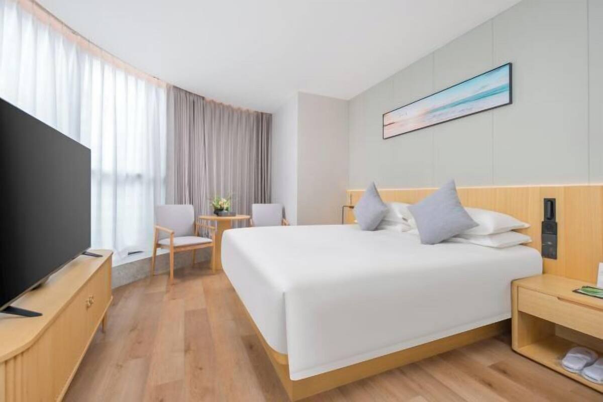 A hotel room with a bed, TV, wooden furniture, and a painting on the wall.