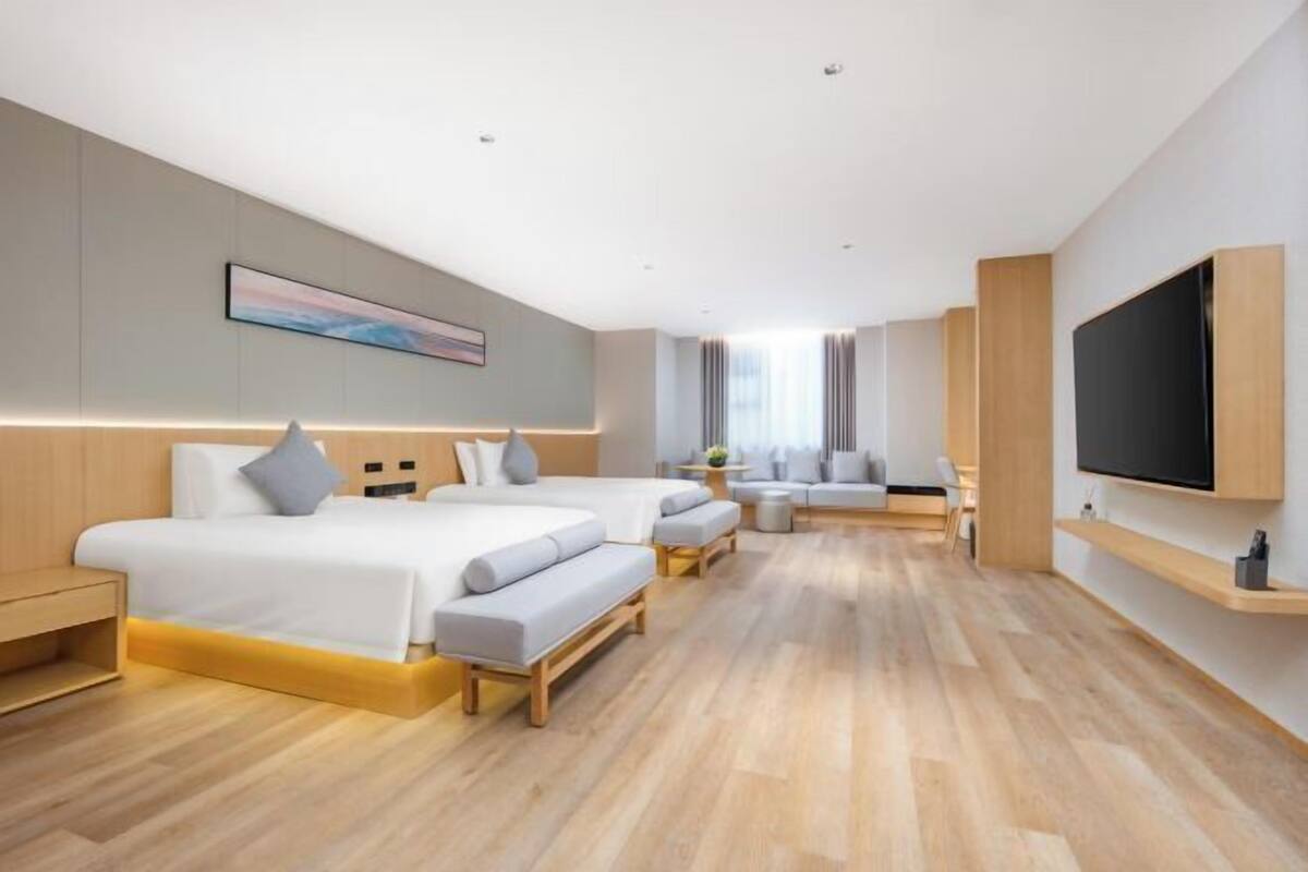 A modern hotel room with two beds, a sofa, a TV, and a desk.