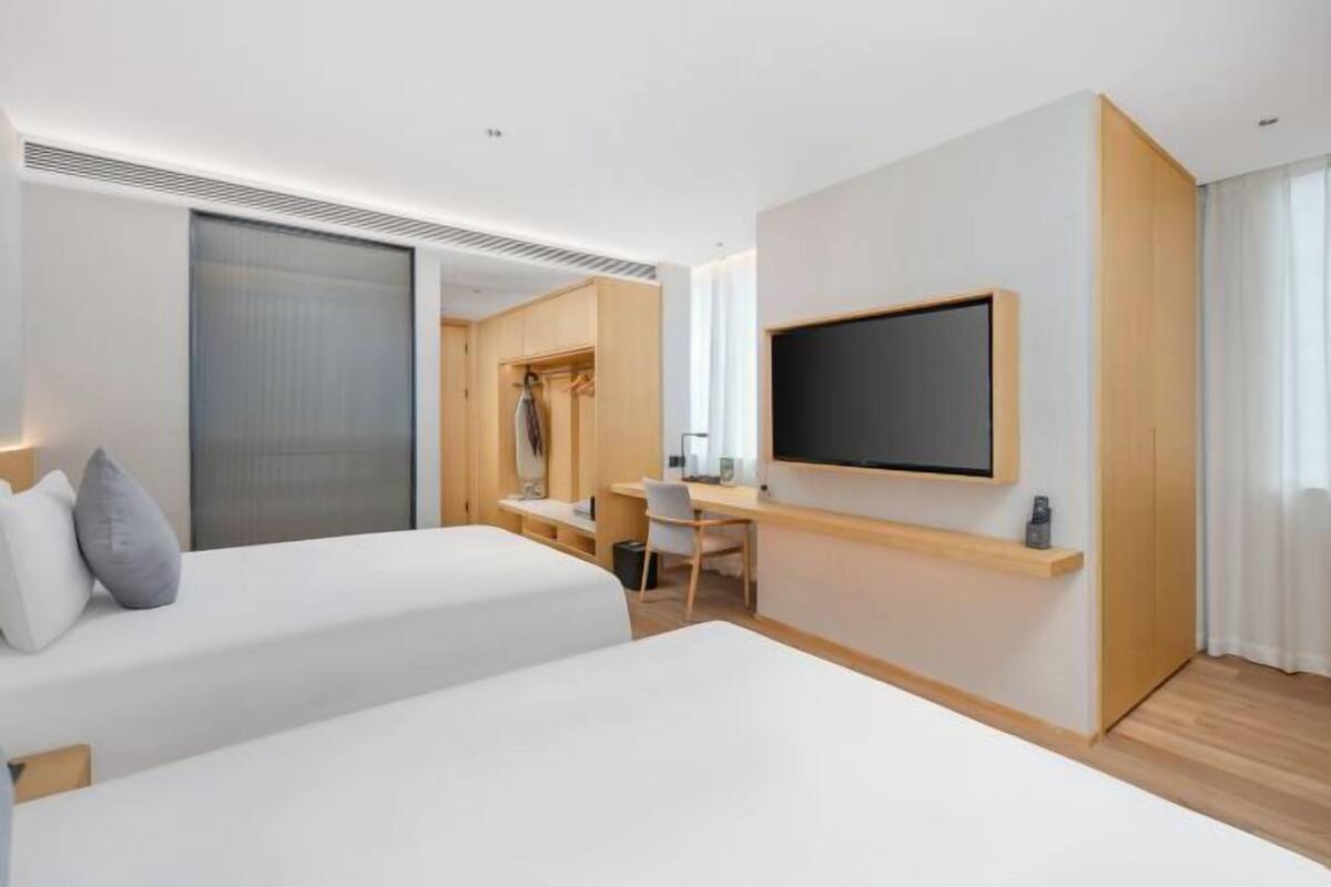 A hotel room with two beds, a desk, a TV, and a sliding door.