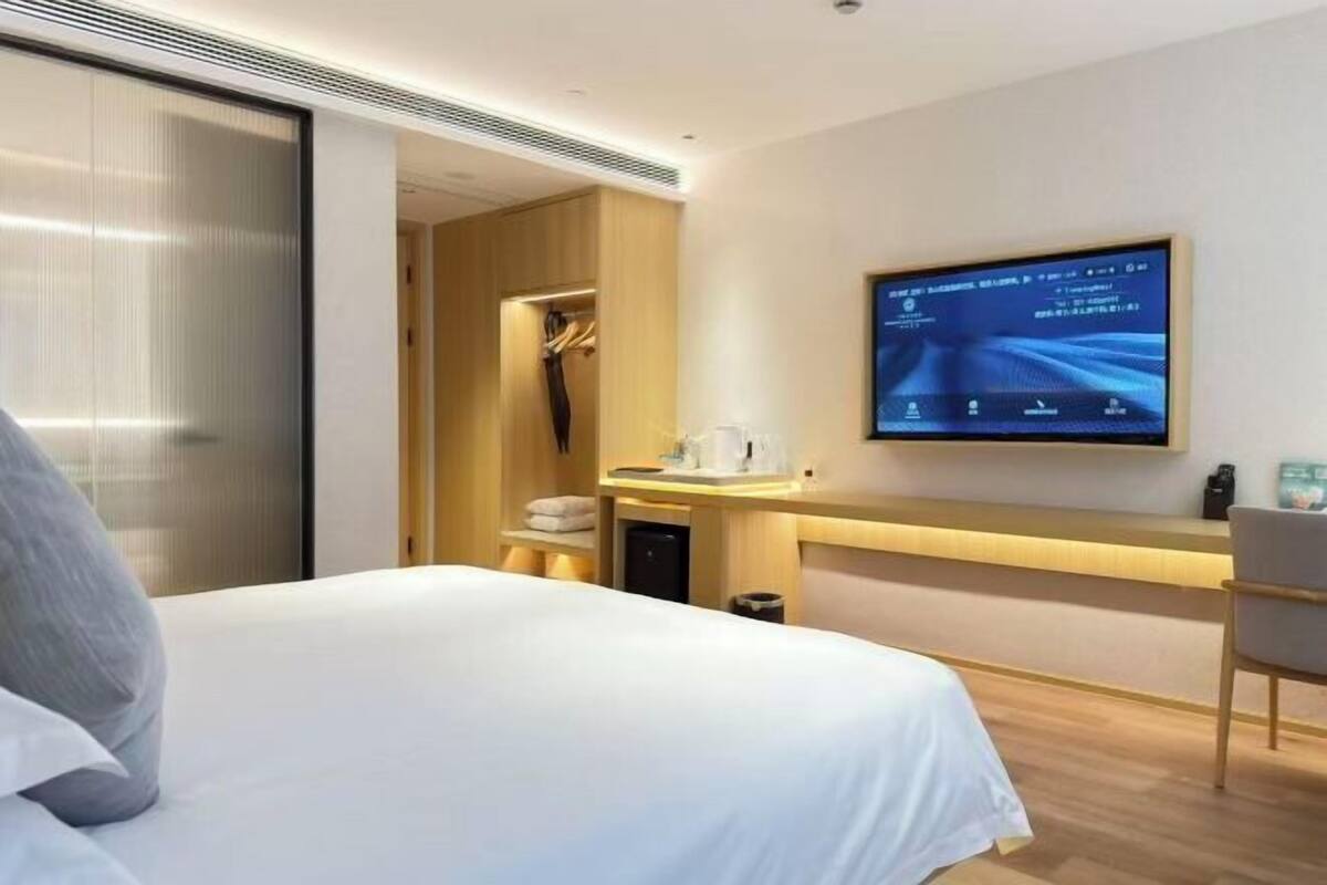 A modern hotel room with a bed, a desk, a television, and a wardrobe.