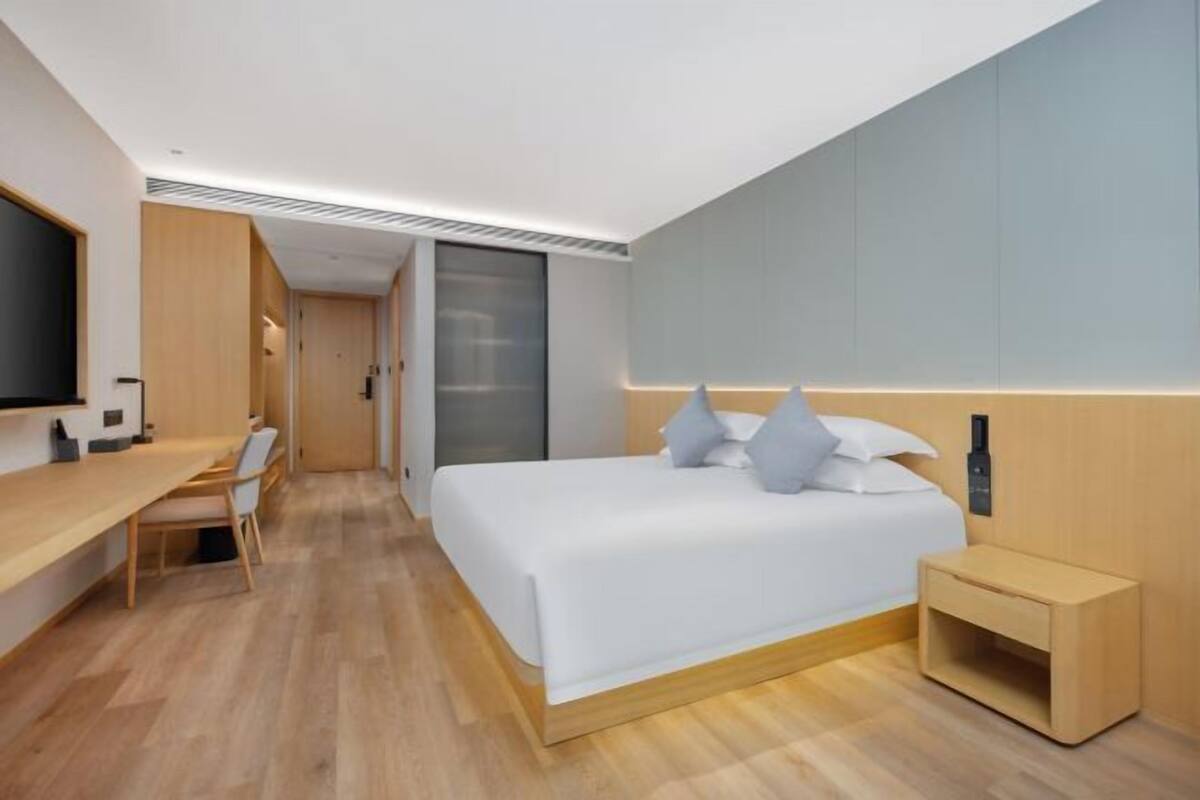 A modern hotel room with a bed, bedside table, and a desk with a chair.