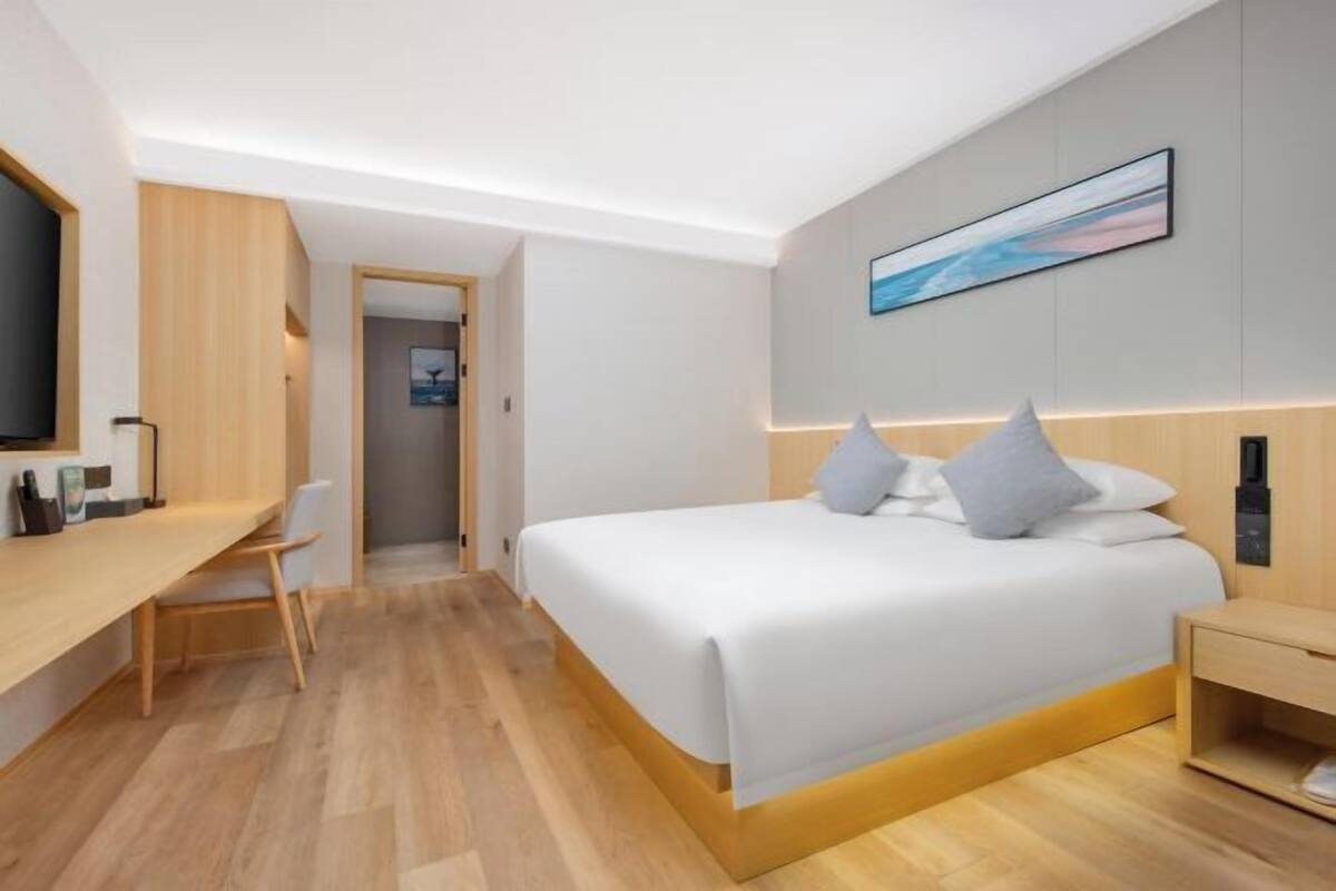 A modern hotel room with a bed, a desk, a chair, and a TV.