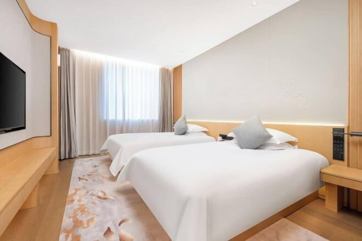 A hotel room with two beds, a flat-screen TV, a large window with curtains, and a wooden floor.