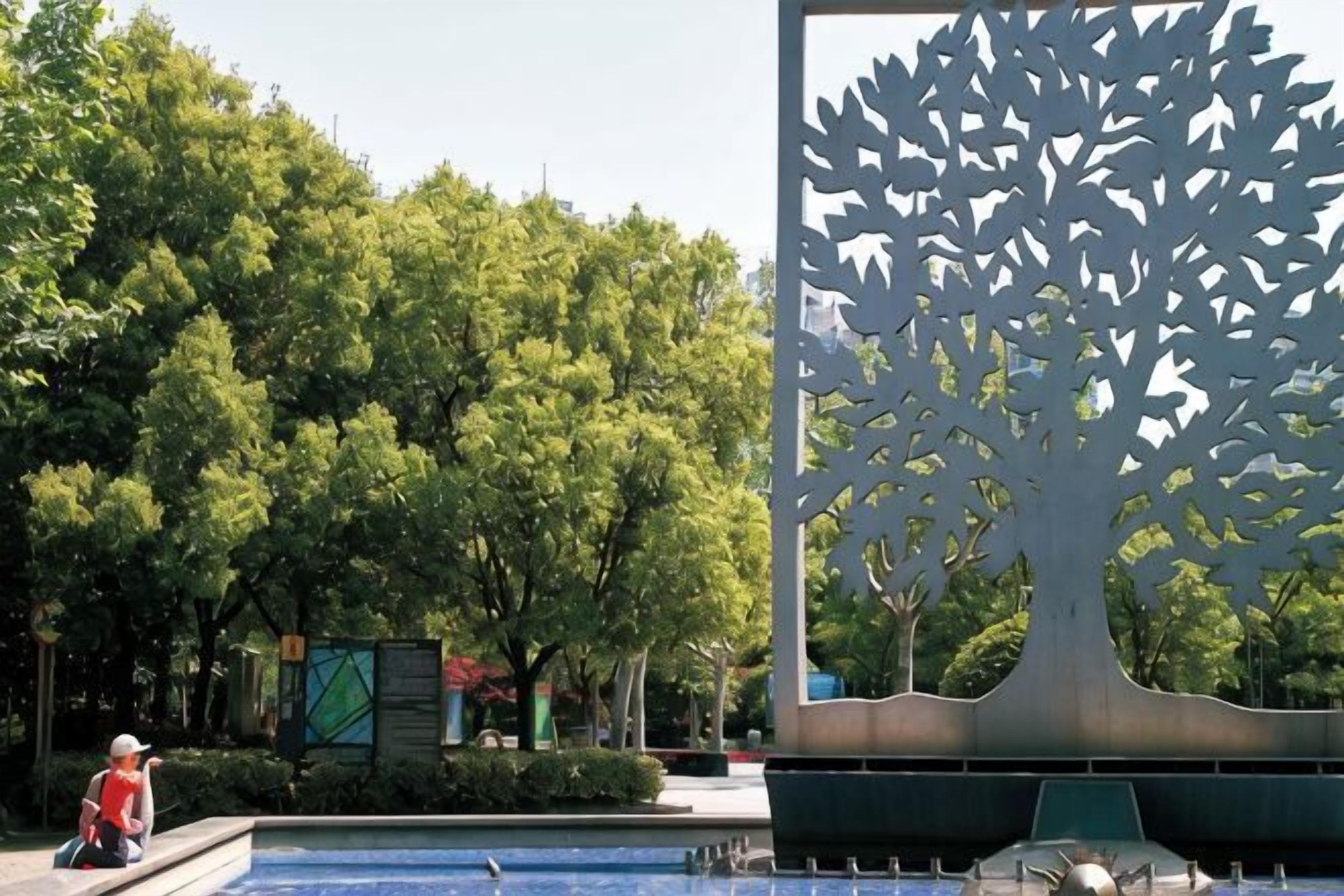 A tree sculpture, a fountain, and a person in a red shirt.