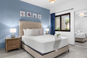 A modern bedroom with a large bed, bedside tables, and a window with curtains. - Brand NEW 2br2ba w Private Pool in Gated Community (Noord)