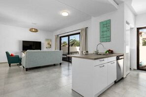 A modern kitchen with a central island, a dining area with a sofa, and a large window with curtains.
