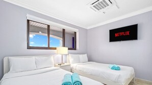 A hotel room with two beds, a window, a wall-mounted TV displaying 'NETFLIX', and a ceiling air conditioner. - 2BR 2BA Duplex w Amazing Views Pool Amenities (Noord)