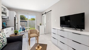 Una sala de estar moderna con un televisor de pantalla plana, un sofá, una mesa de centro y un comedor con una mesa y sillas.
