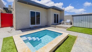 Una casa moderna con piscina, un garaje rojo y un patio con mobiliario exterior.