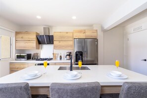 Een moderne keuken met witte aanrechtbladen, houten kastjes en roestvrijstalen apparatuur, plus een centraal eiland met zitplaatsen.