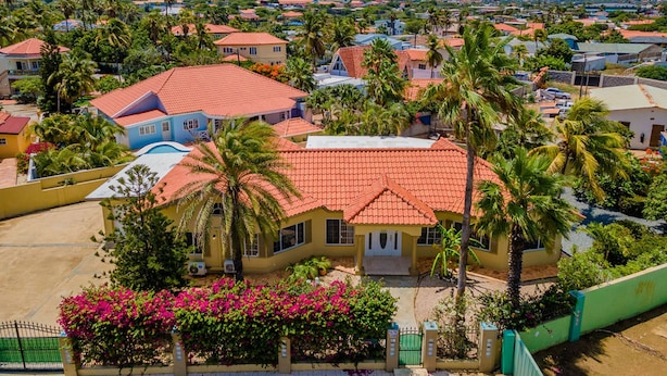Zona residencial con casas de techo rojo, rodeada de abundante vegetación y palmeras.